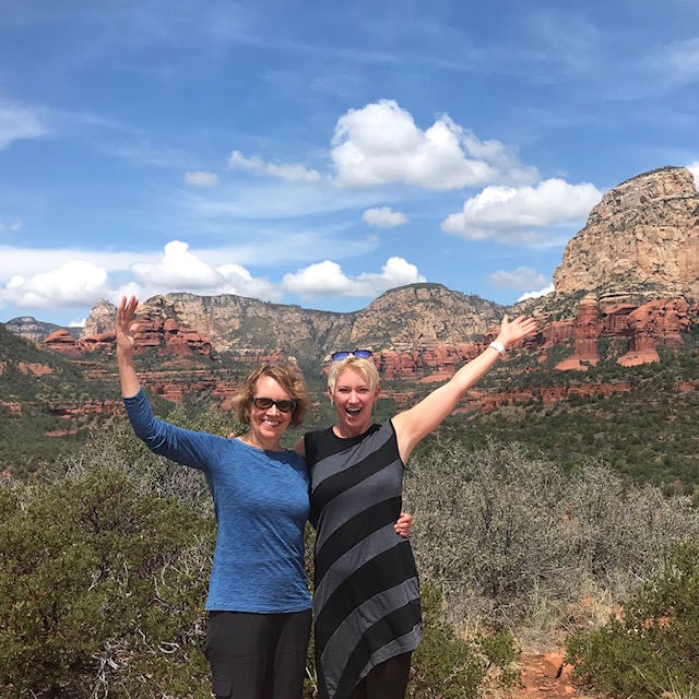 Two women celebrating outdoors with Sedona red rock formations in the background